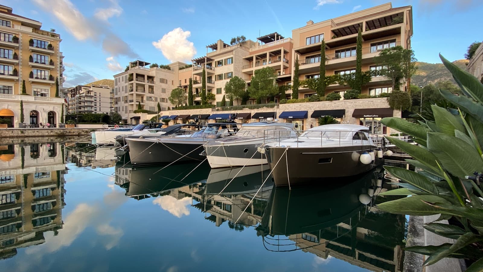 A marina lined with docked motor yachts in front of waterfront residential buildings at golden hour.