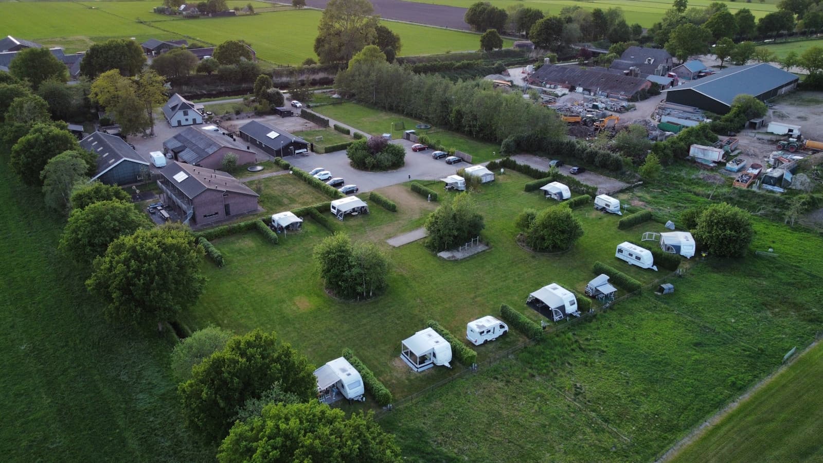 An aerial view of a small countryside campground with several RVs on hedged sites.