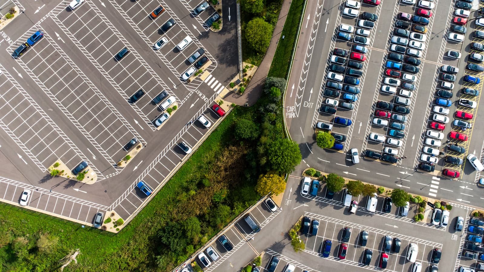Aerial view of a large parking lot filled with rows of parked cars, too distant for any plate or logo to be readable, with no people visible.