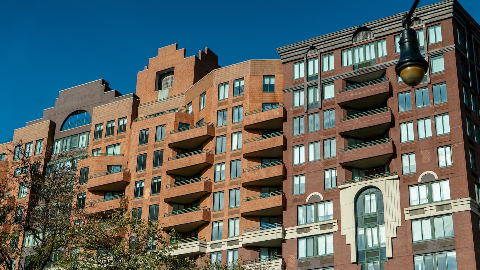 A multi-story brick apartment building with rows of windows and balconies, photographed from below against a blue sky, with no people or text visible.