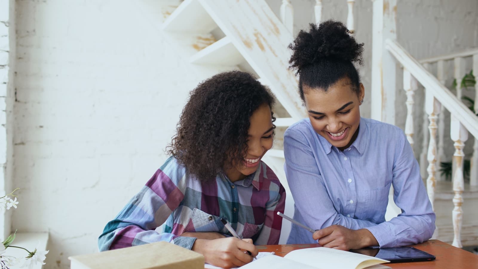 Two young women smiling and studying together at a table with notebooks.