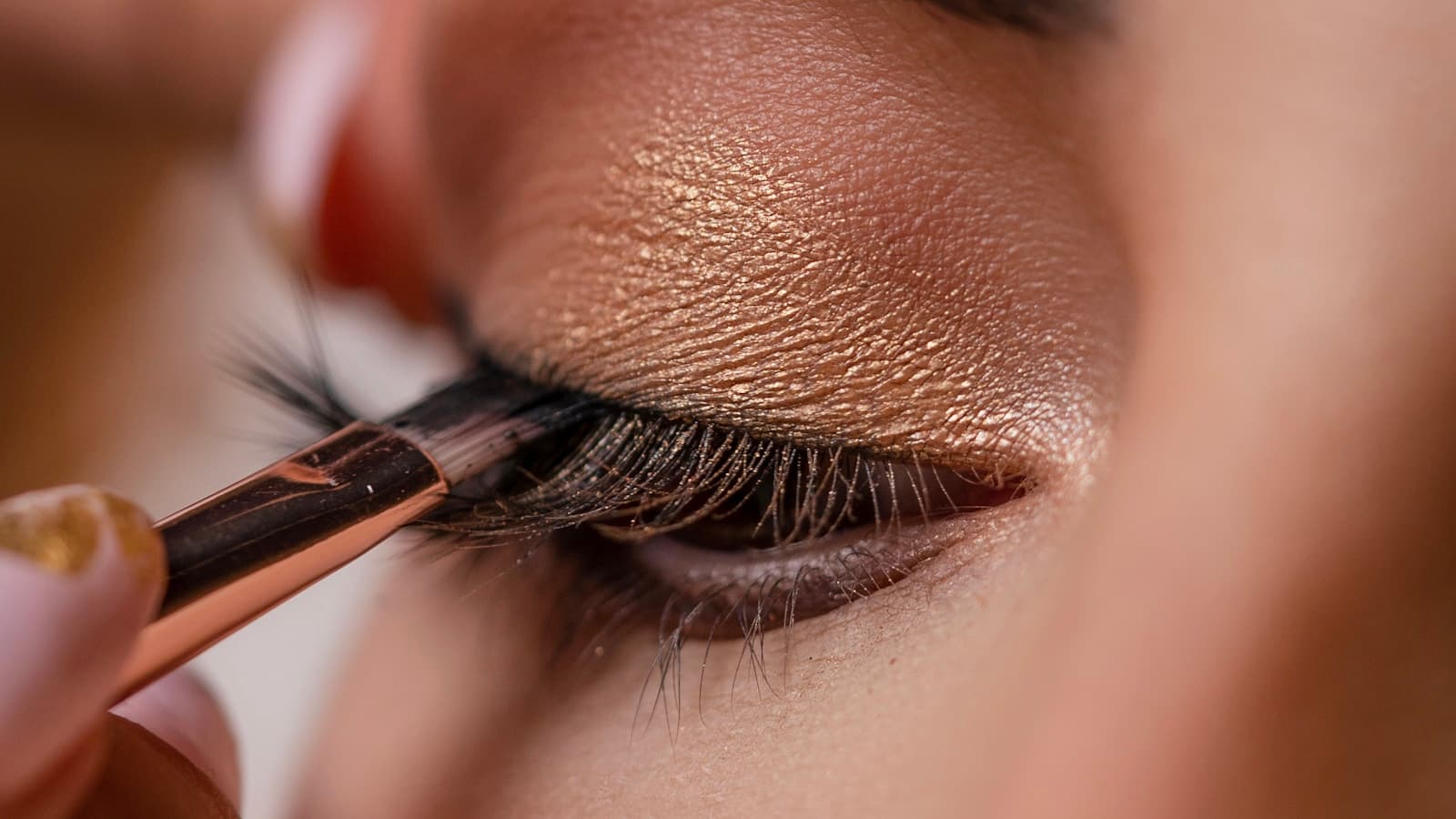 Extreme close-up of a makeup artist applying eyeshadow and false lashes to a model's eye.