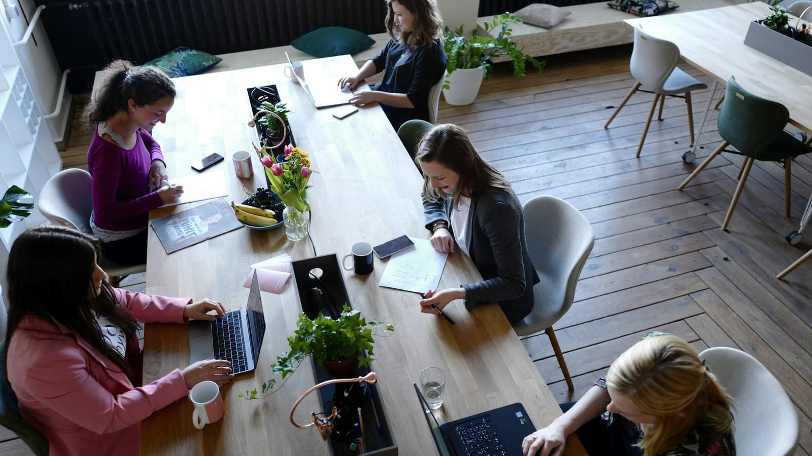 A group of people gathered around a wooden table in a shared workspace.