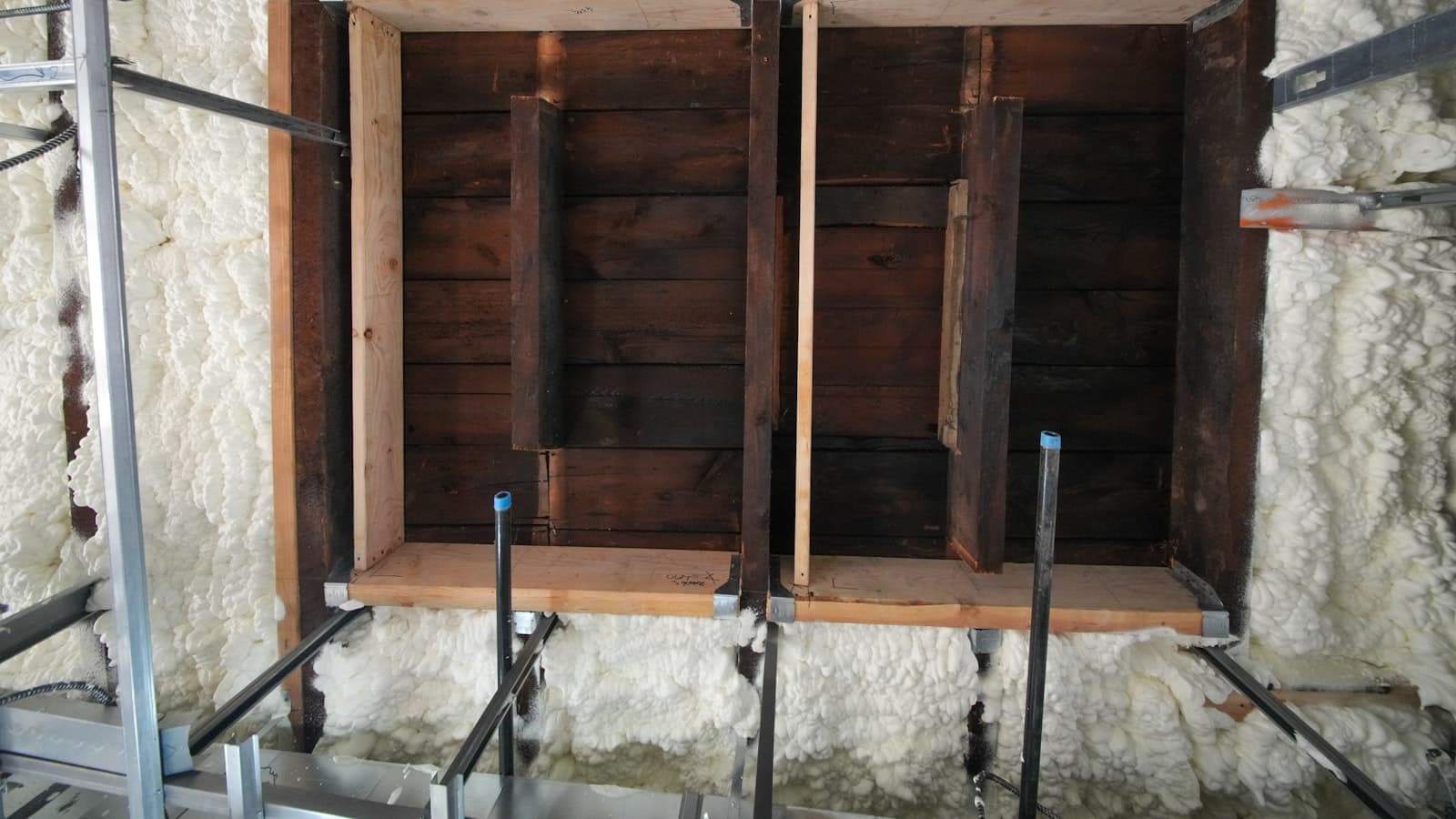Overhead view of wood floor joists sprayed with white foam insulation during a home construction project, no people or text.