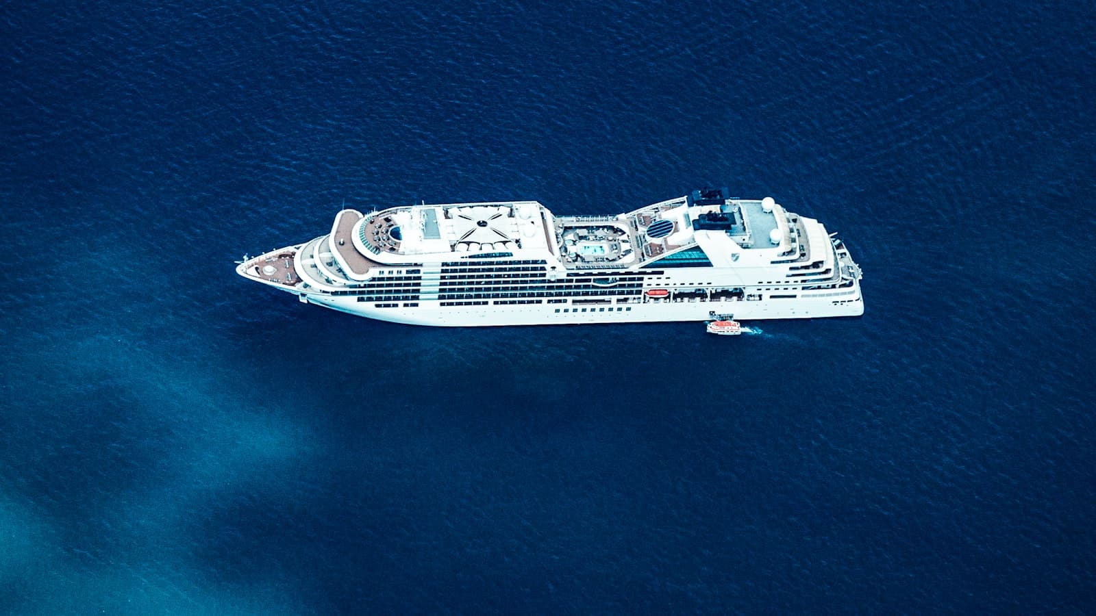 Aerial view of a white cruise ship on deep blue water, with no readable ship name, logo, or people visible.