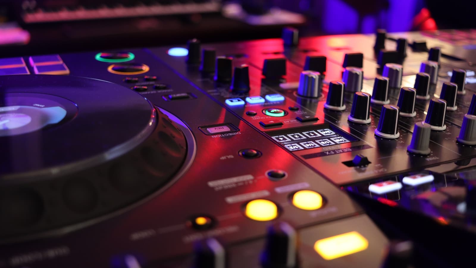 Close-up of a DJ mixer and controller lit in purple and blue with glowing jog wheels.