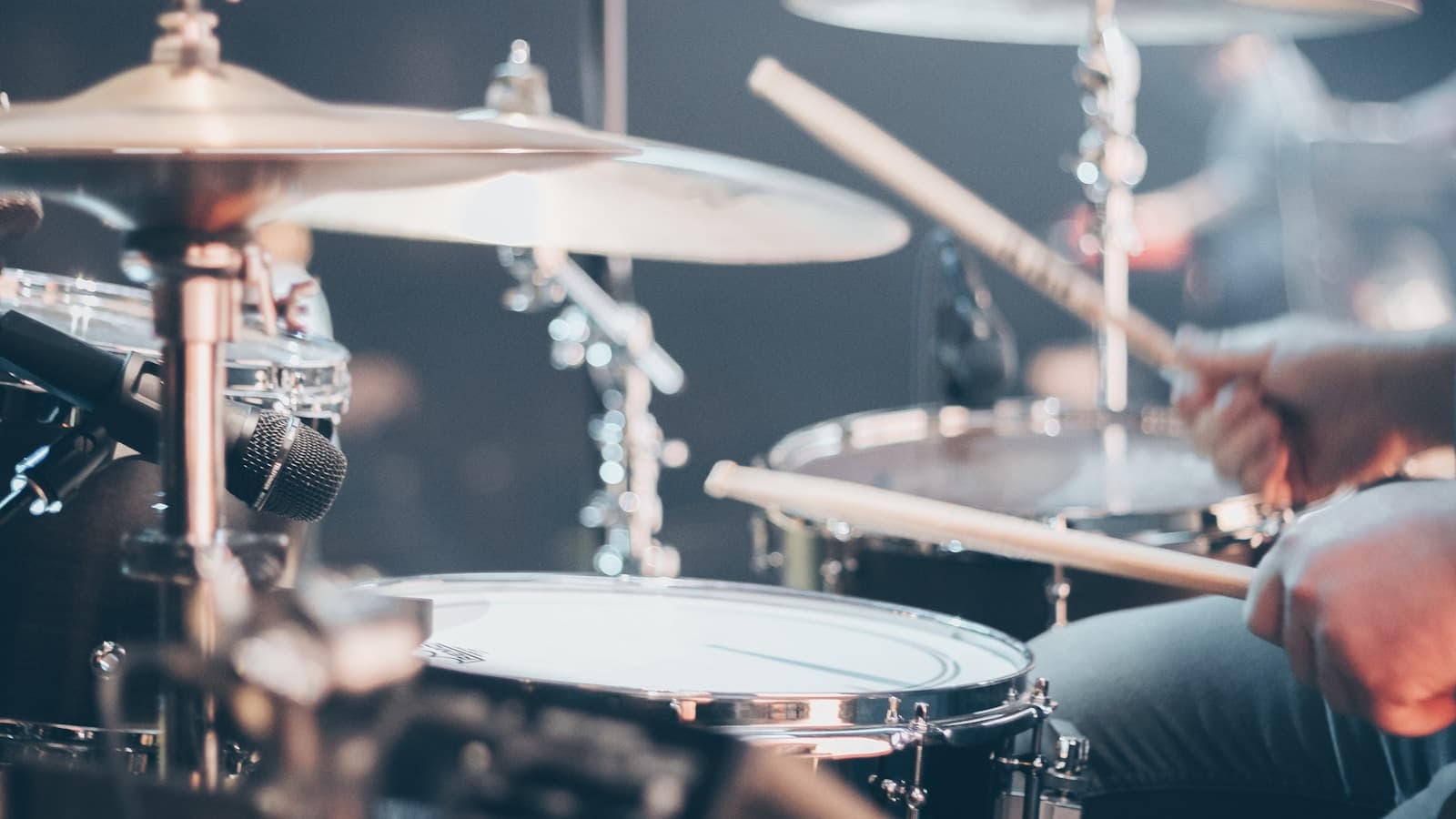 A drum kit lit warmly on a stage at a live show, cymbals and toms in focus.
