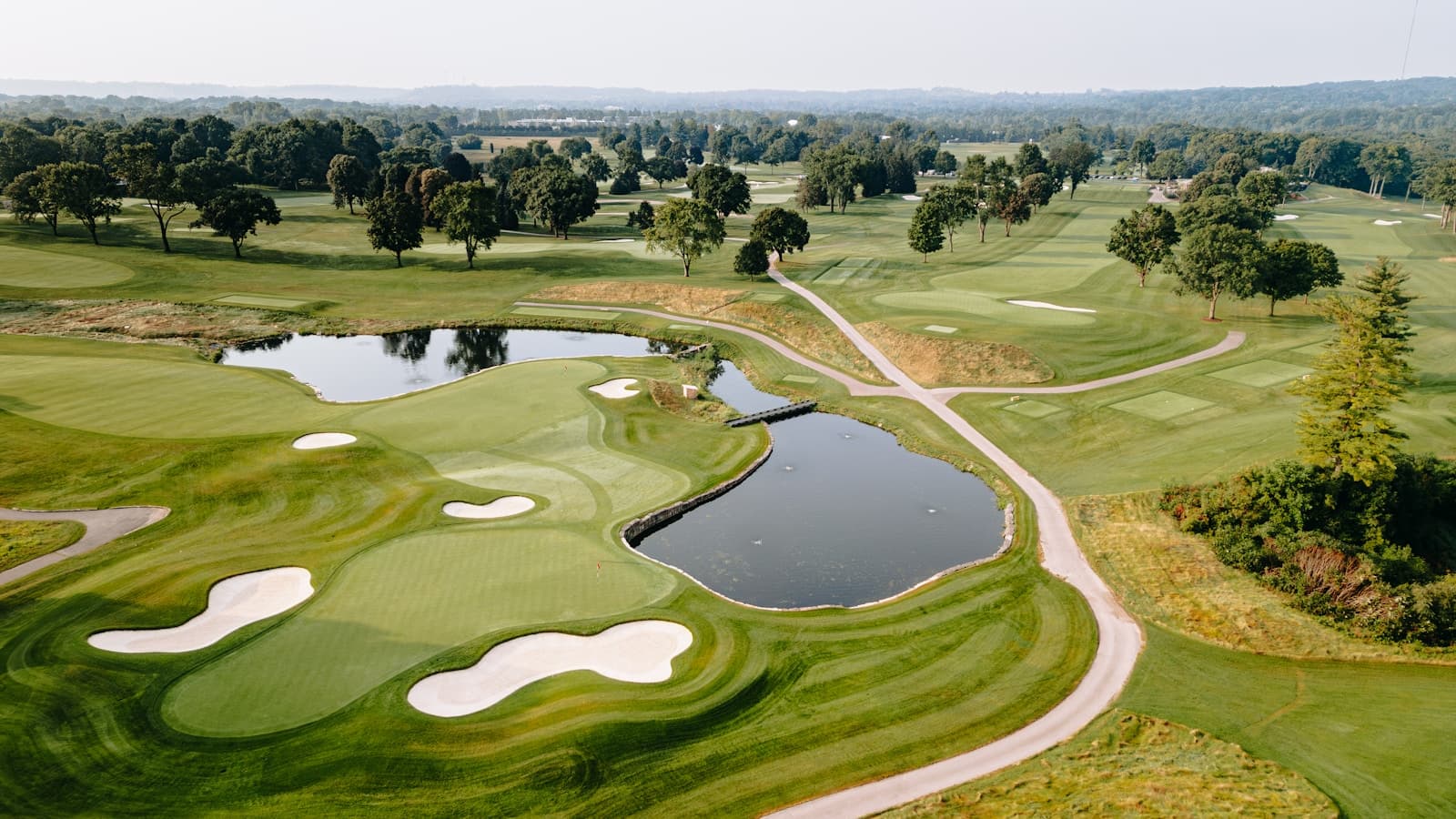 Aerial view of manicured golf greens, sand bunkers, and a pond at a club.