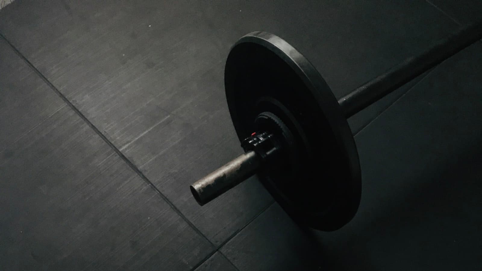 A close-up of a black weight plate and barbell on a dark gym floor, no readable text, logos, or people.