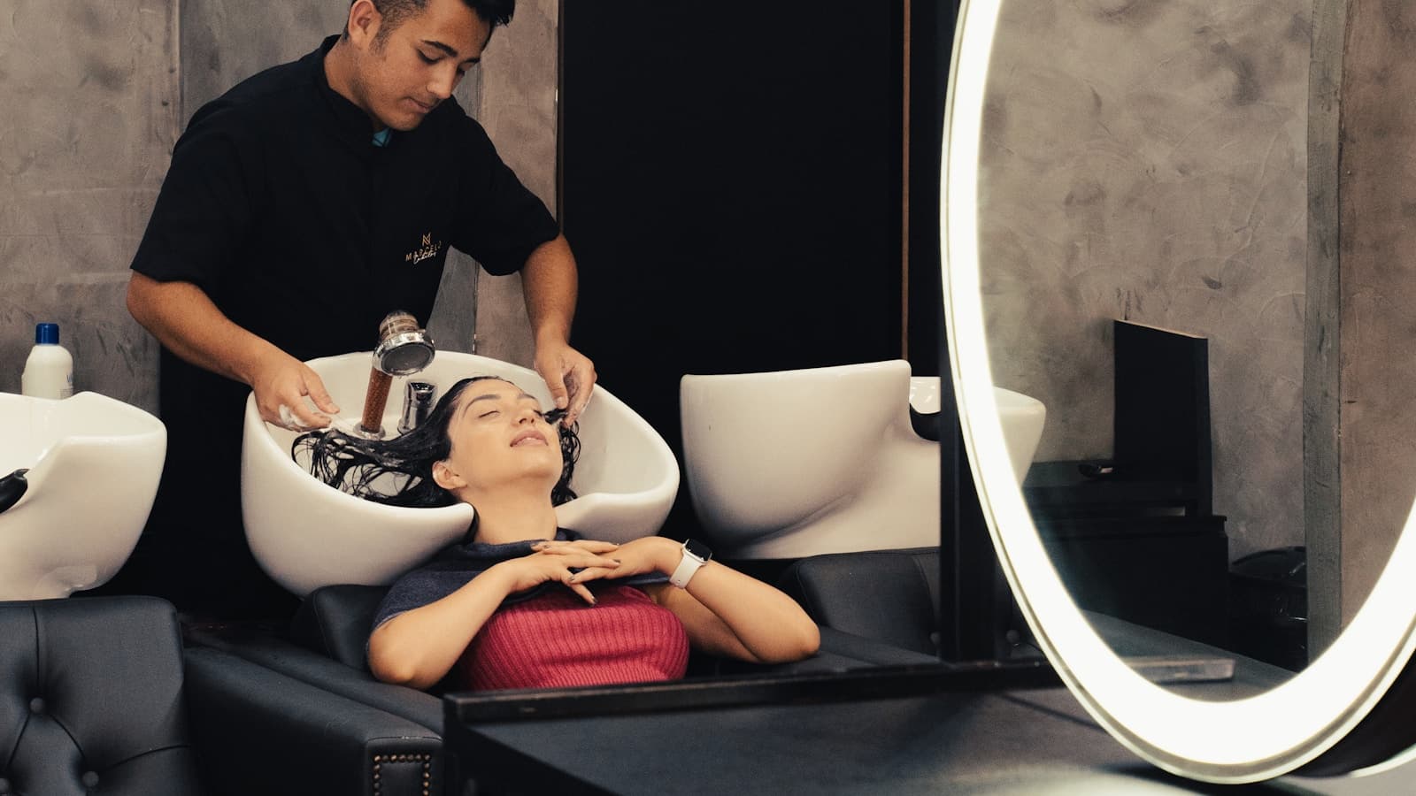 A barber washing a client's hair at a salon basin.