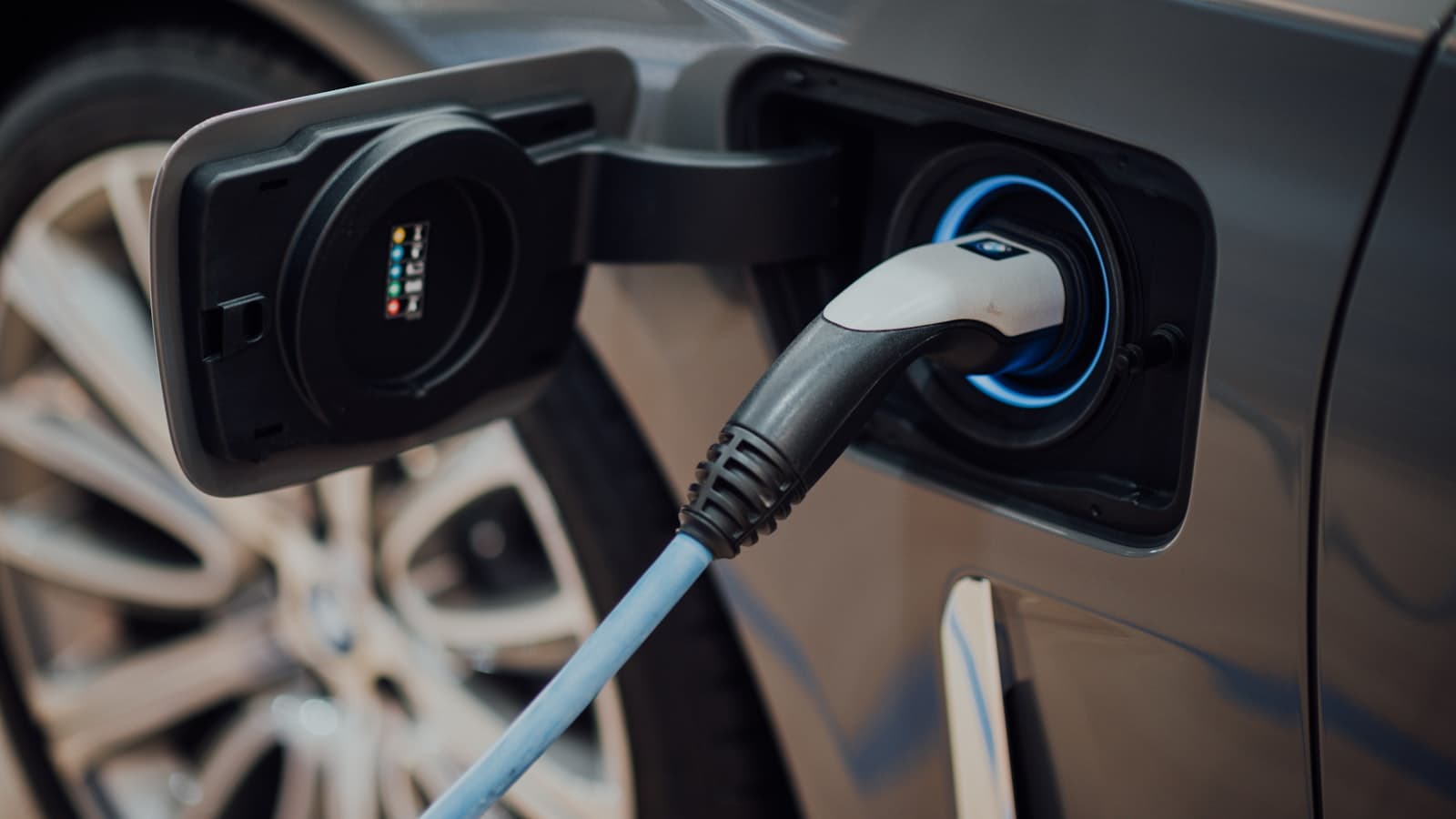 Close-up of a charging cable plugged into a gray car's charge port, with no visible plate, logo, or people.