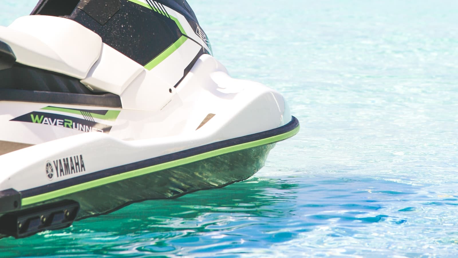 Close-up of a white, black, and green jet ski's bow resting on shallow turquoise water, no people, text, or logos visible.