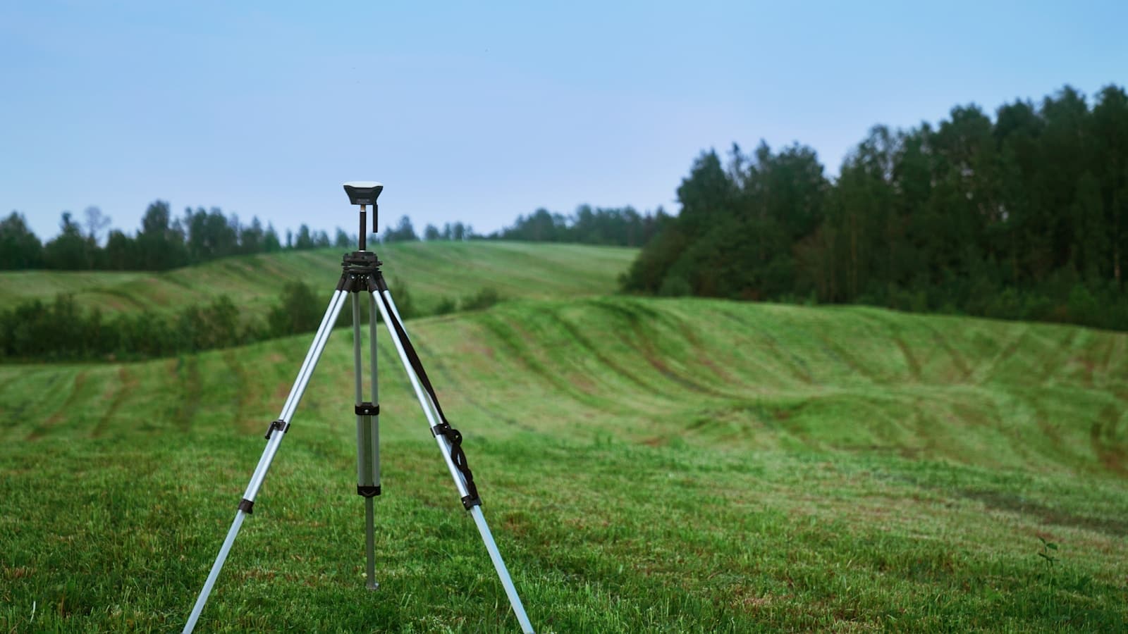 A surveying tripod and GNSS receiver alone in a green grass field.