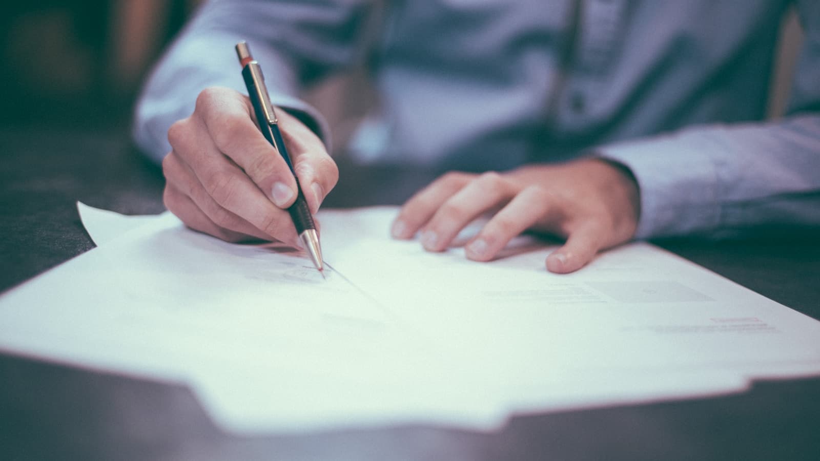 Close-up of a hand signing paperwork at a desk.