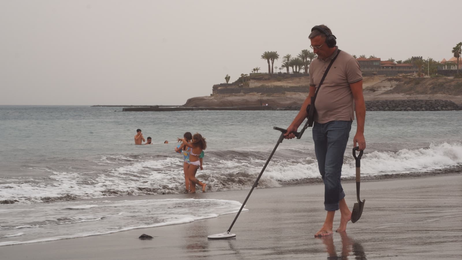 A man using a metal detector on a sandy beach in daylight.