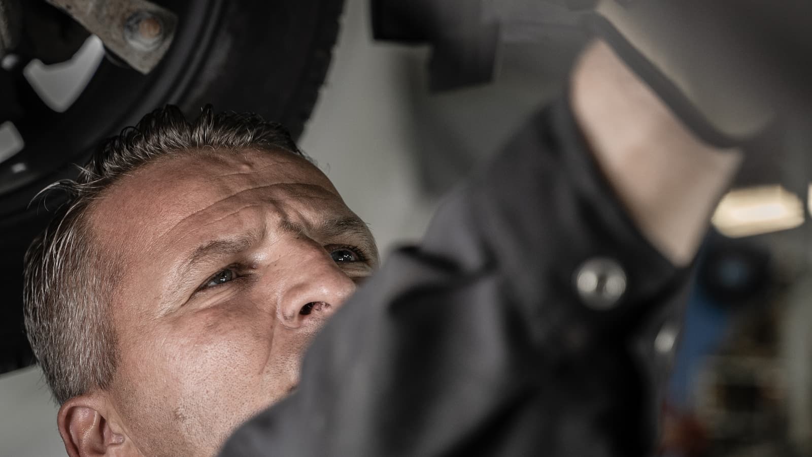 A mechanic looking up while working underneath a car's chassis.
