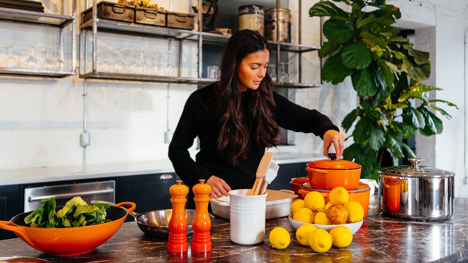 A woman preparing healthy food with lemons and greens in a bright modern kitchen.