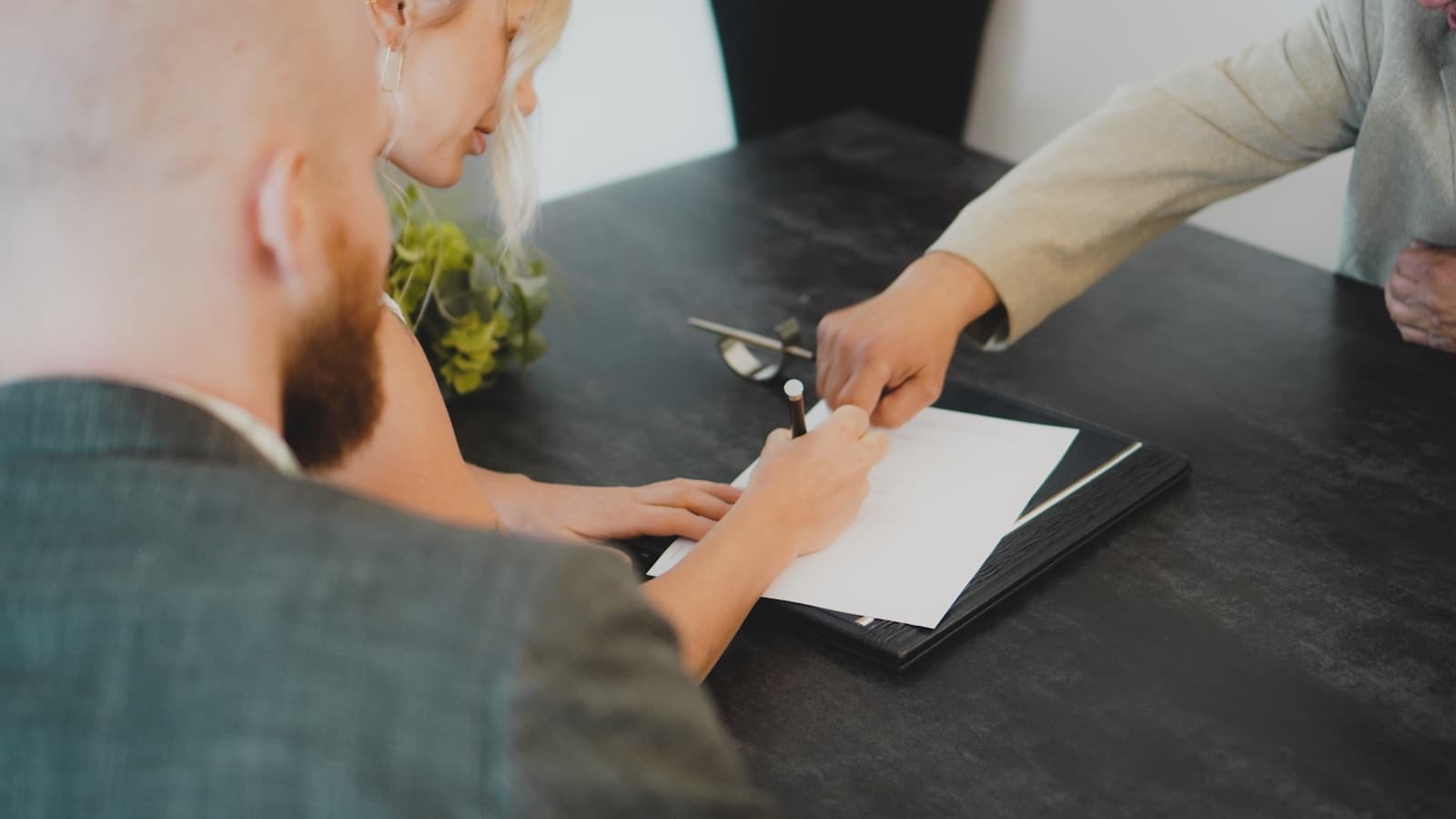 A couple signing a document together at a desk, papers blurred and unreadable.