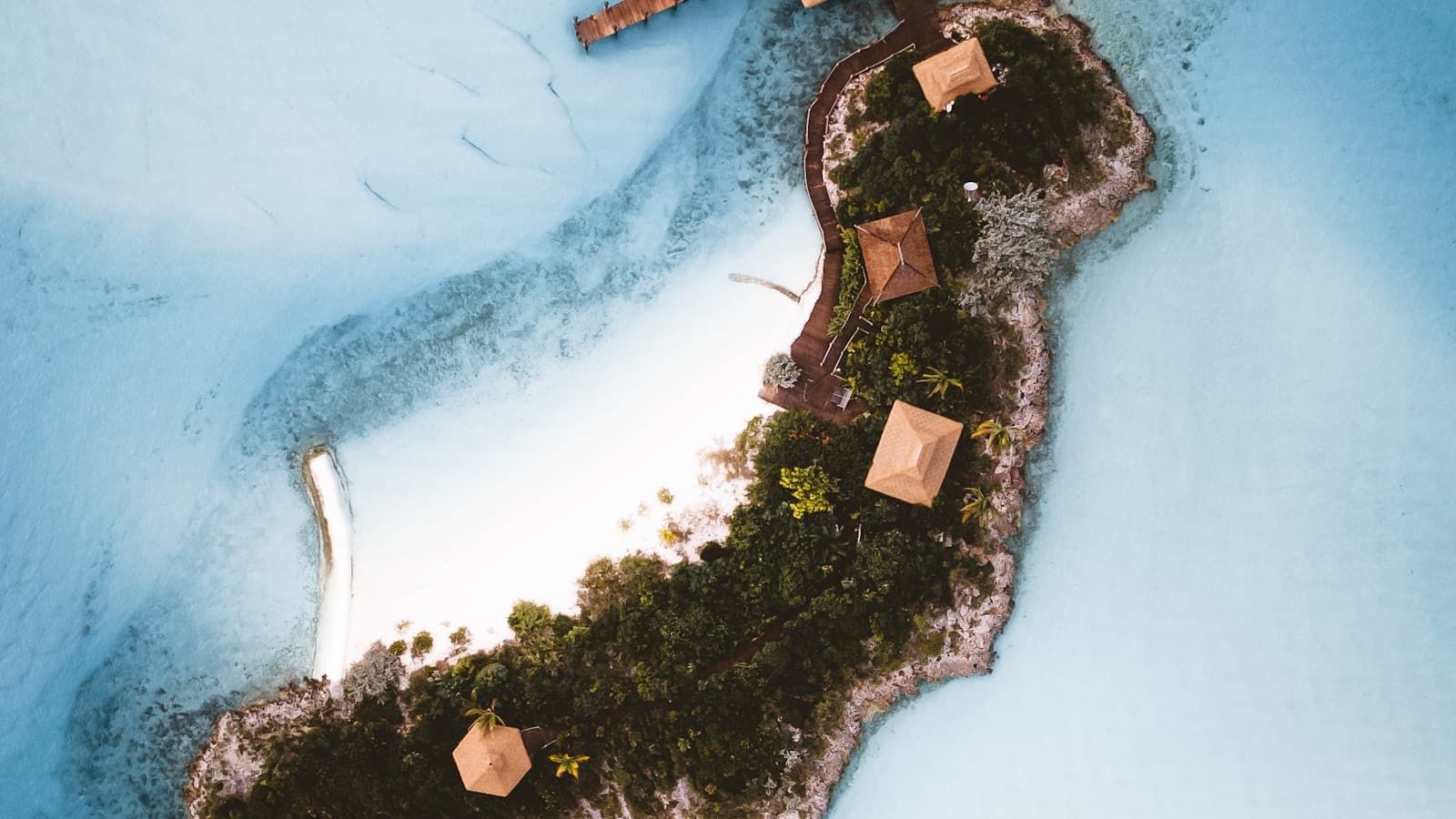 Aerial view of a tiny private island with a few thatched-roof huts and a dock.