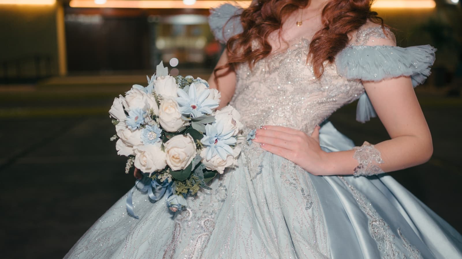 Close-up of a young woman in a light blue, sparkling quinceañera ball gown holding a bouquet of white and blue flowers.