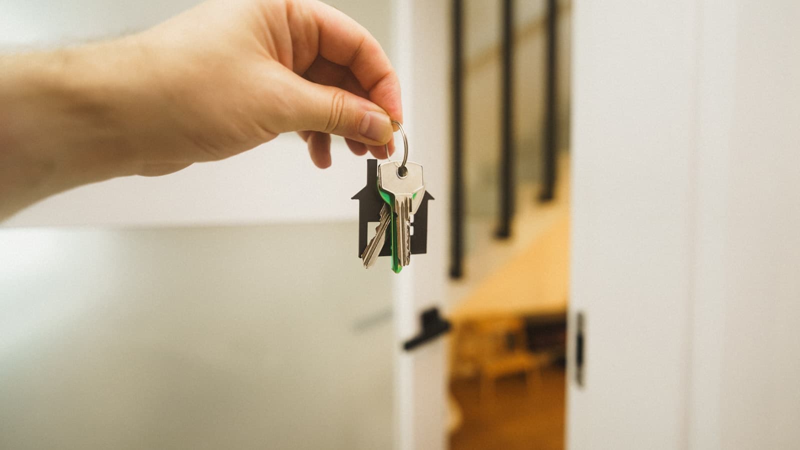 A hand holding a house-shaped keychain with keys in front of an open door.