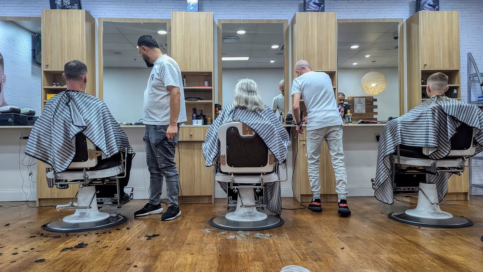 A modern barbershop with stylists working at three chairs along a mirror wall.