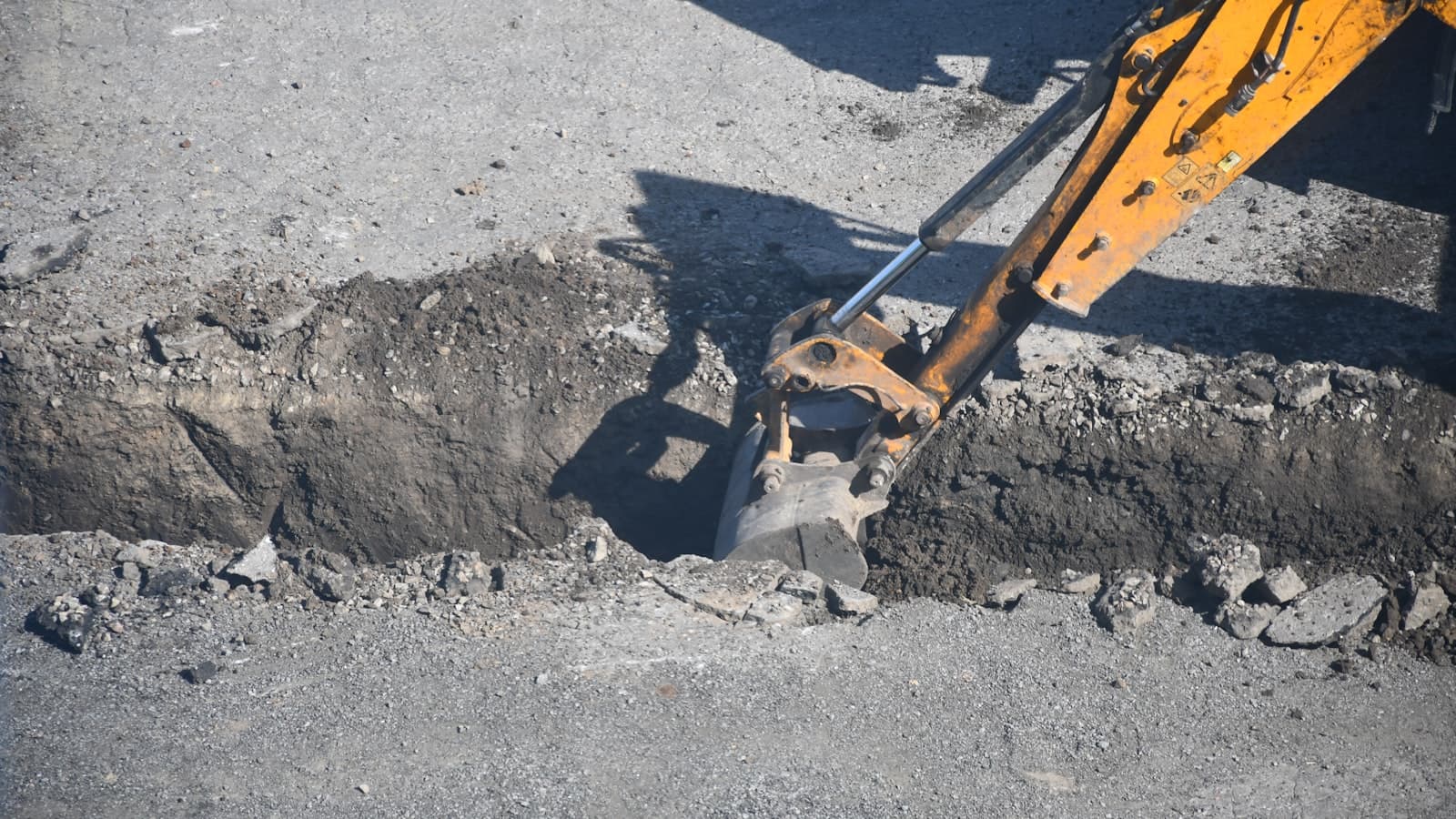 An excavator bucket digging a trench in the ground, representing septic system excavation work; no faces or readable text.