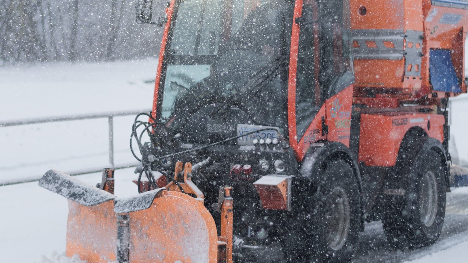 An orange snowplow blade clearing a snowy road, front-on shot.