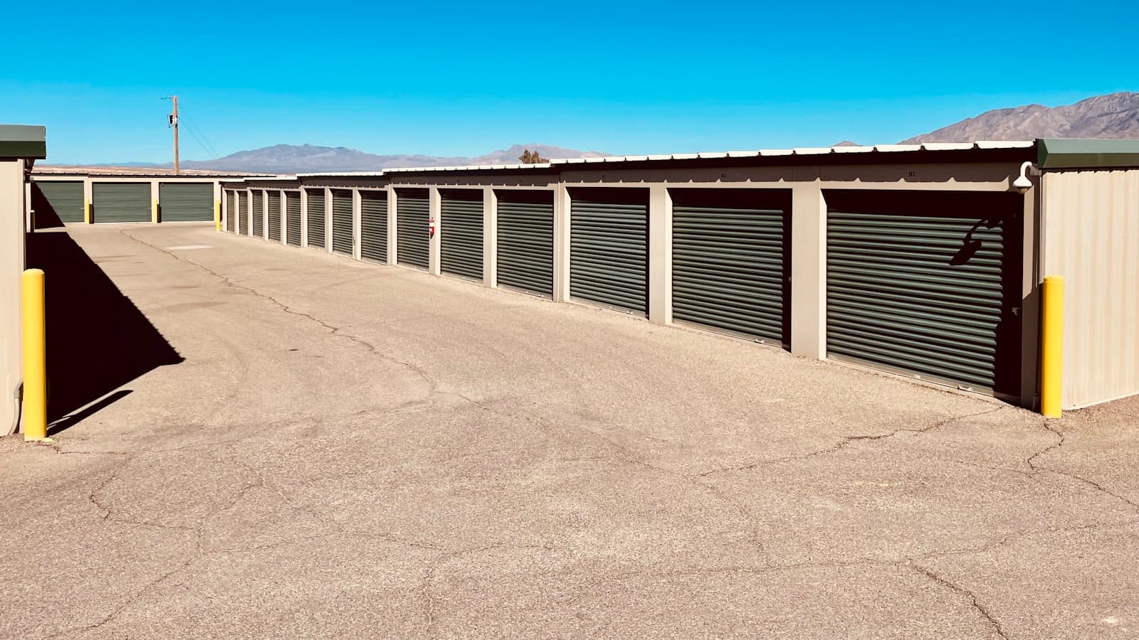 A row of self-storage units with roll-up doors under a blue sky, with no people or readable signage visible.