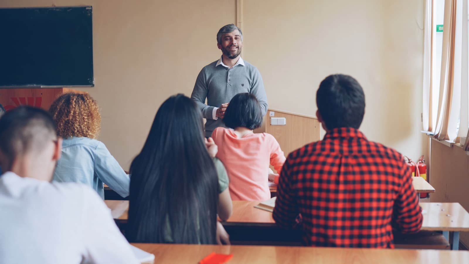 A smiling teacher standing in front of a seated classroom.