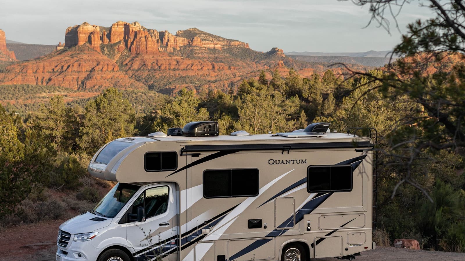 A white RV/travel trailer parked roadside with forest and mountain scenery.