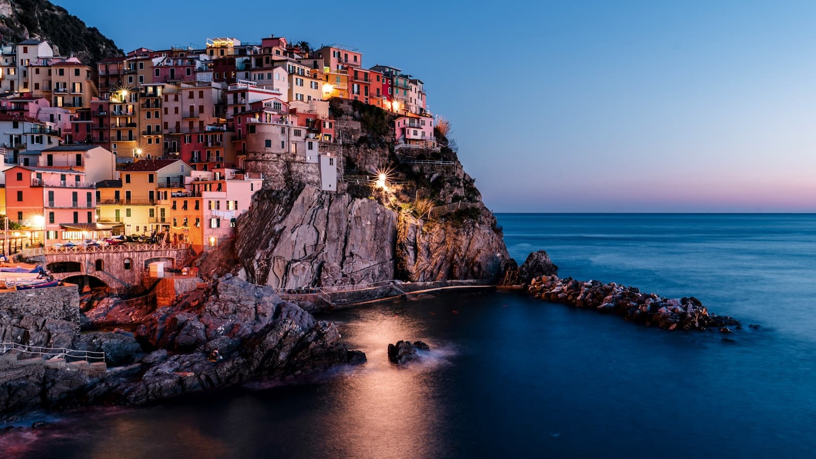 A Cinque Terre-style cliffside village glowing at dusk above the sea.