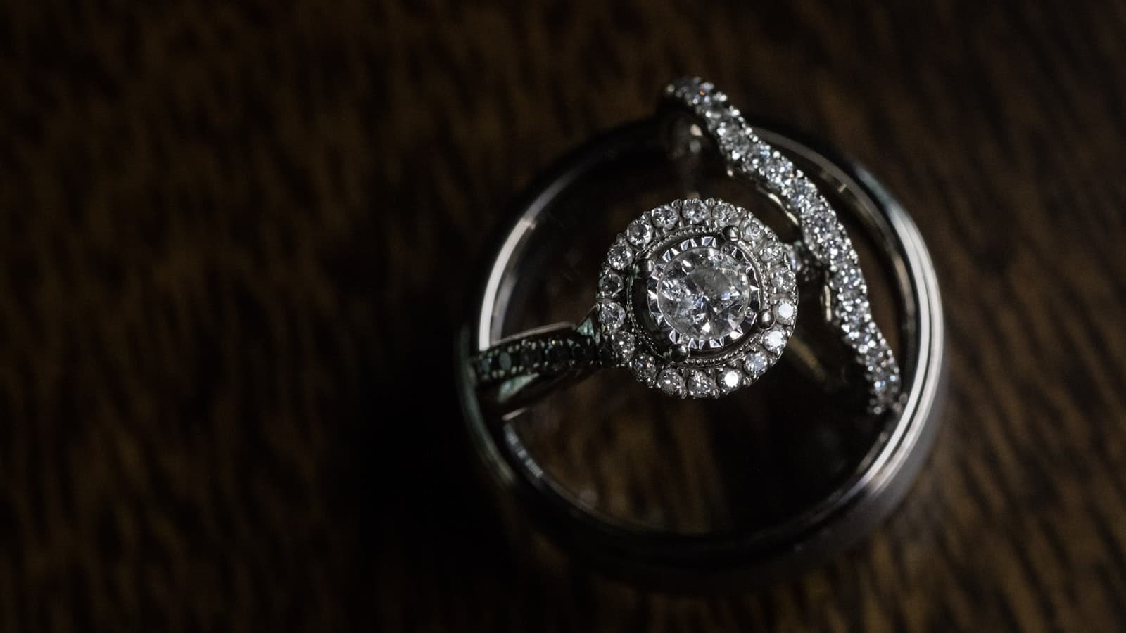 Close-up of a diamond engagement ring resting on a dark textured fabric surface, no people or text.