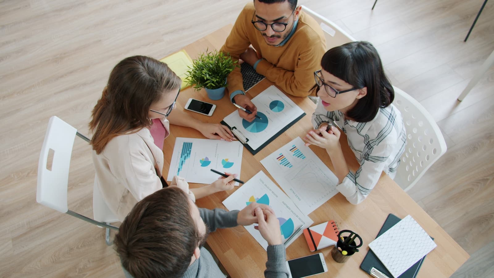Four people around a table reviewing charts and documents, overhead angle.