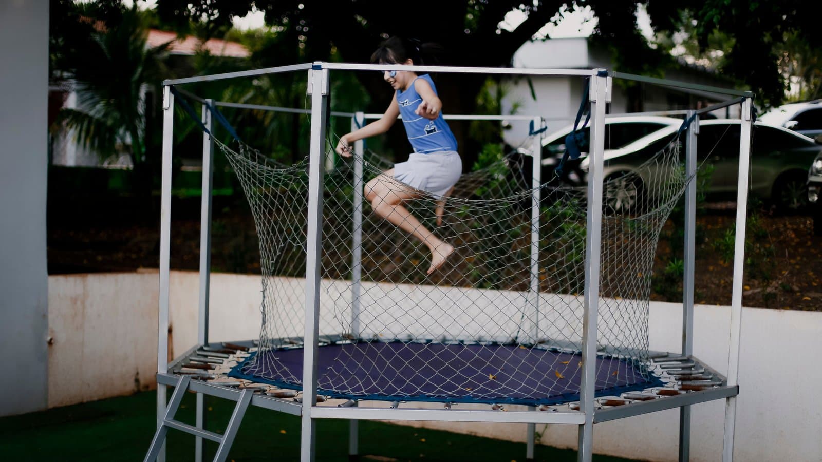 A boy jumping on a framed backyard trampoline with a safety net.