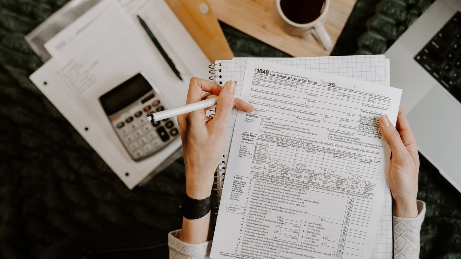Hands filling out a blank tax form with a calculator and coffee nearby.