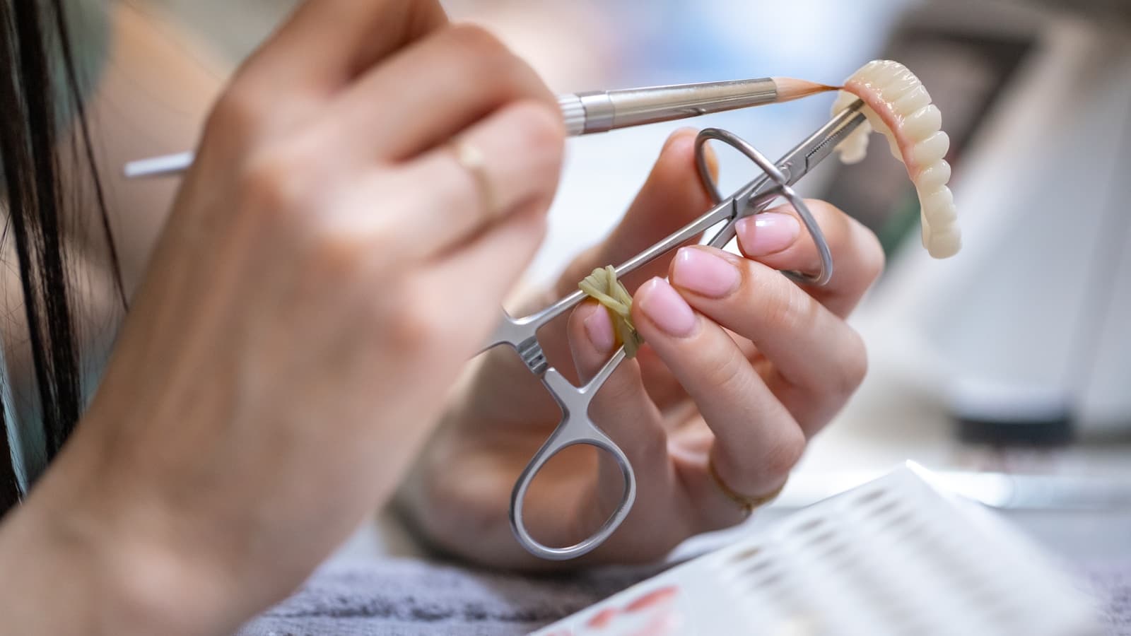 Close-up of hands crafting and adjusting a denture with dental tools.