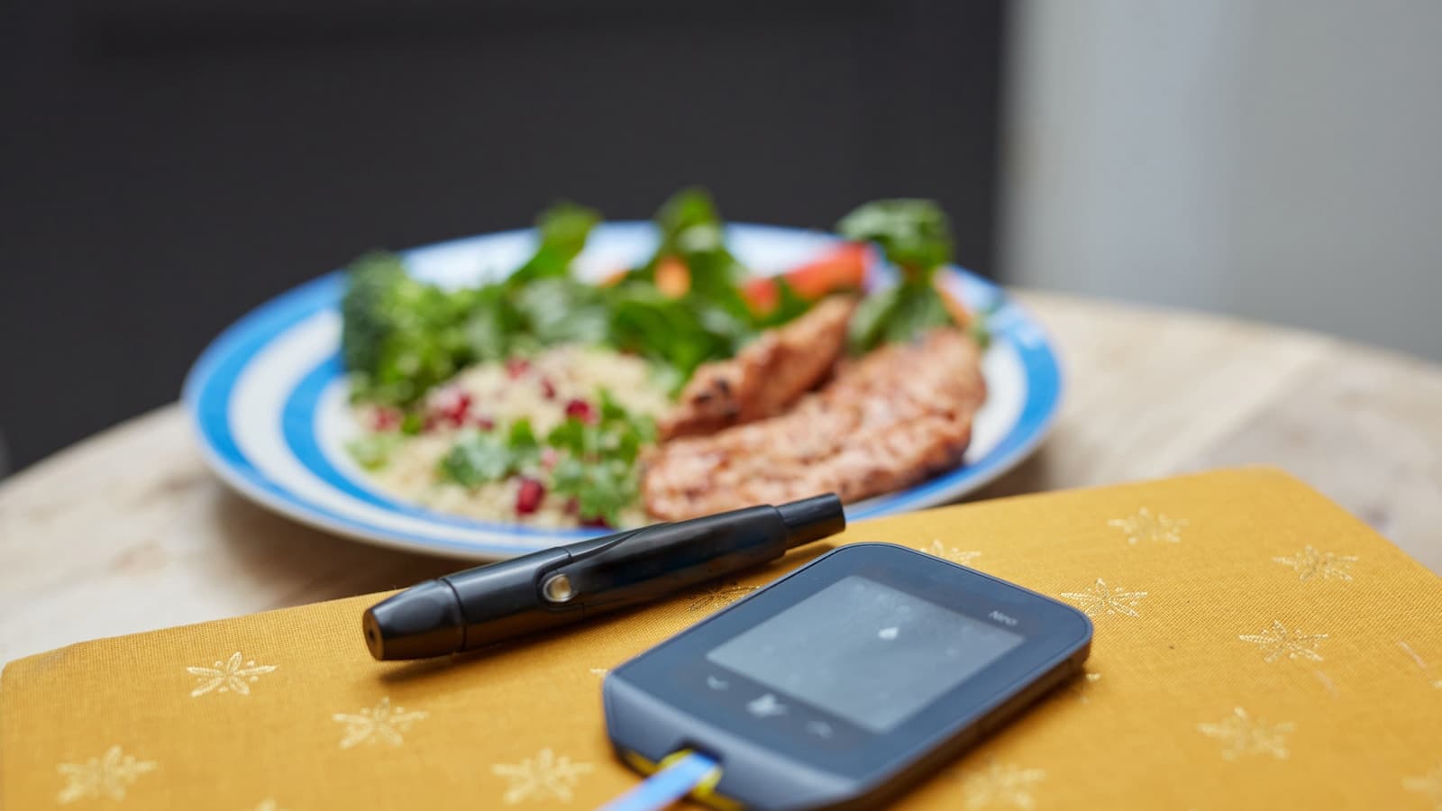 A glucose meter and lancing pen next to a healthy plated meal.