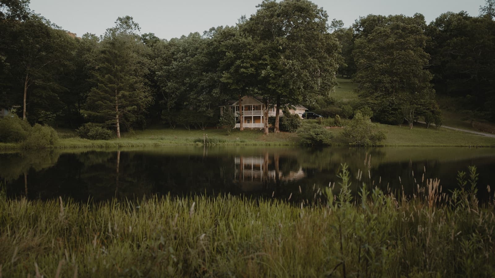 A calm house tucked among trees beside a still lake at dusk.