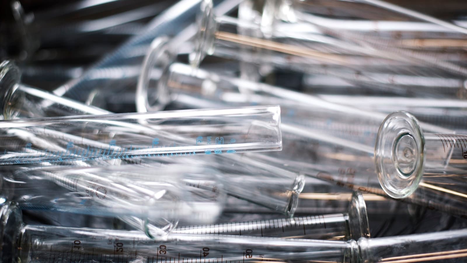 A pile of clear glass laboratory graduated cylinders/test tubes, no people, faces, or readable text.