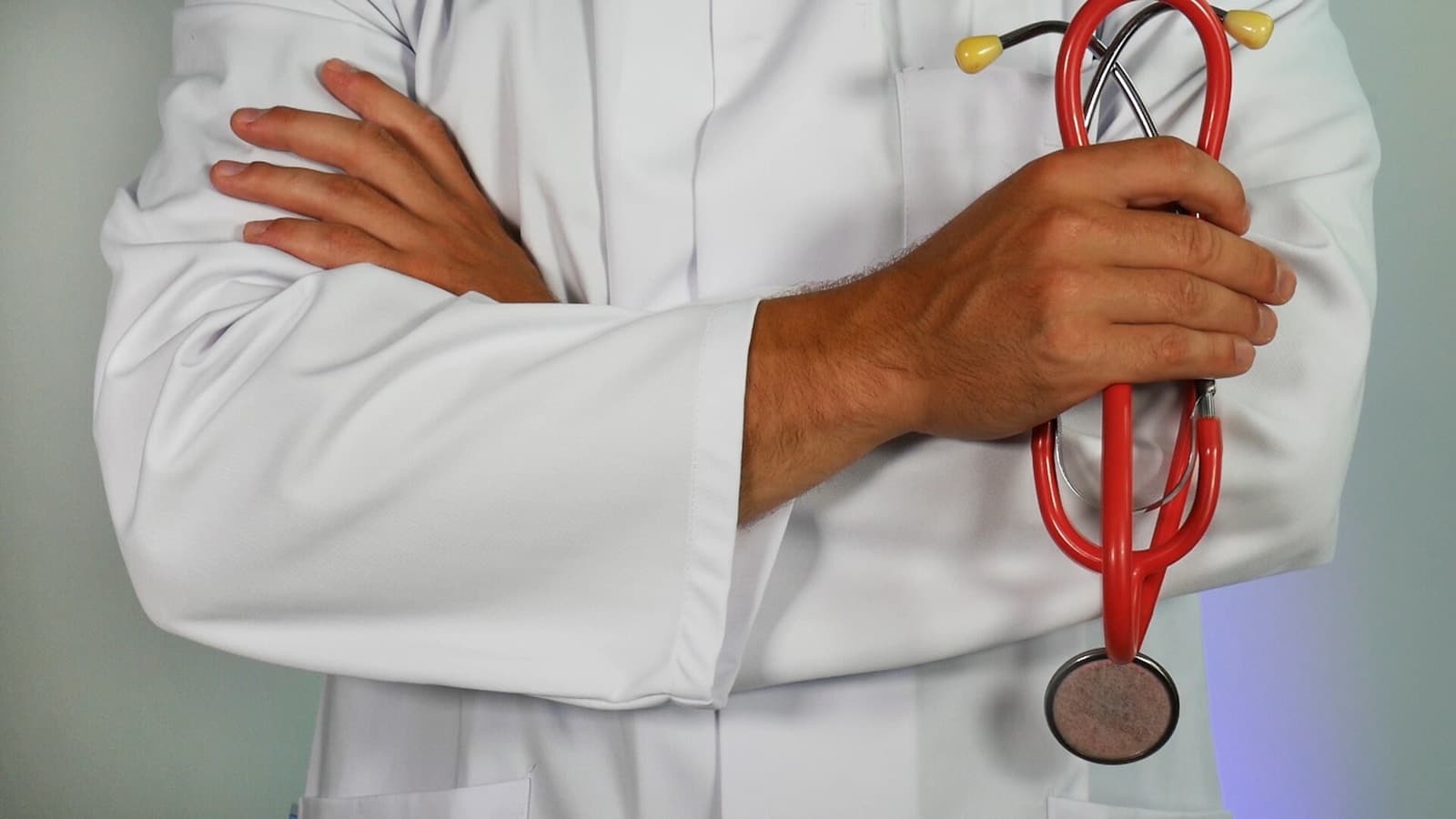 A stethoscope draped over a doctor's white coat, arms crossed.