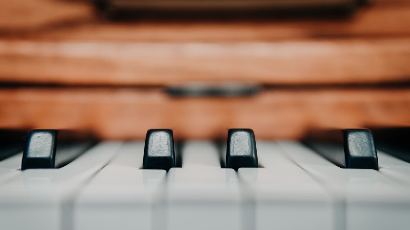 Close-up, selective-focus shot of piano keys with a warm wooden piano body in the background, no people, text, or logos.