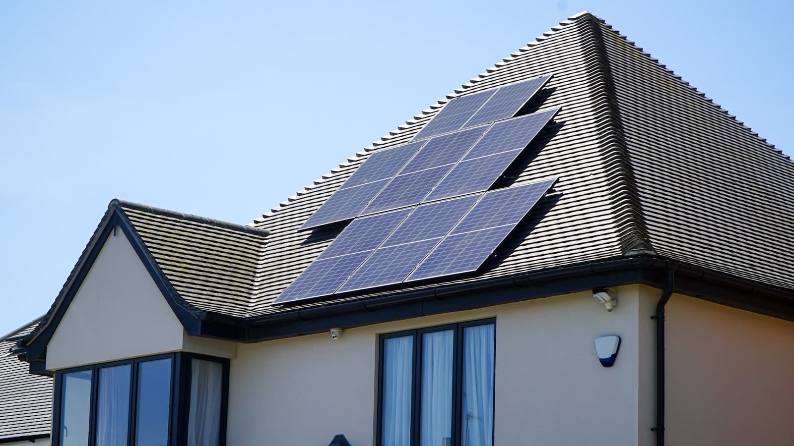 A residential house with a rooftop solar panel array under a clear blue sky, no people or text visible.