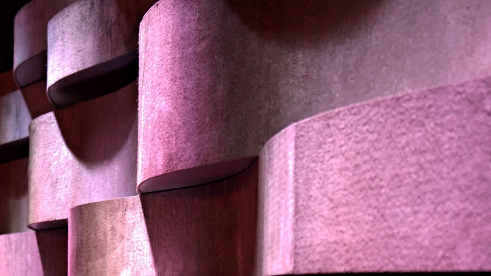 A close-up of curved acoustic foam panels on a studio wall under purple lighting, no people, text, or logos.