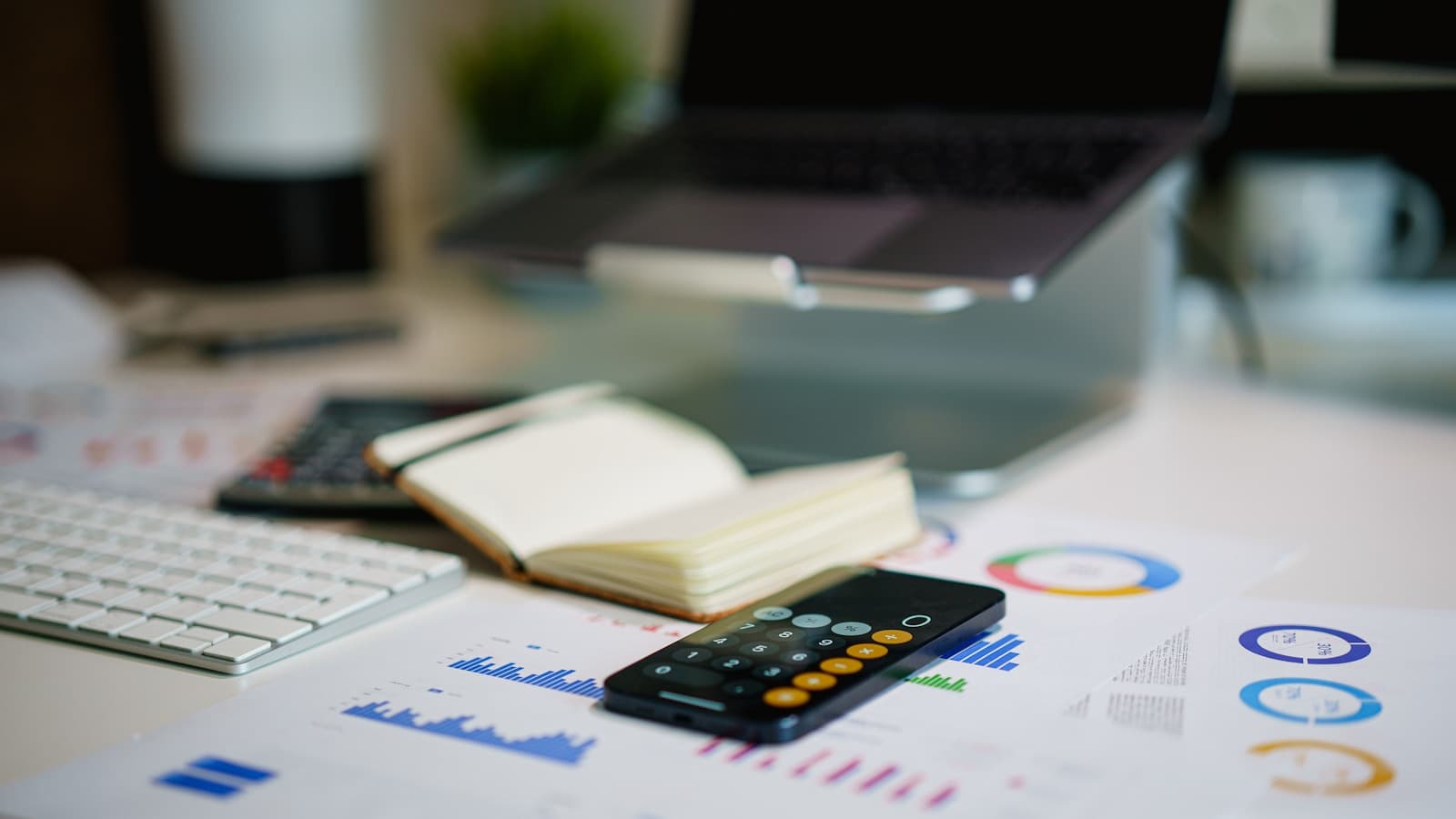 A desk scene with a calculator app on a phone resting on printed financial charts.