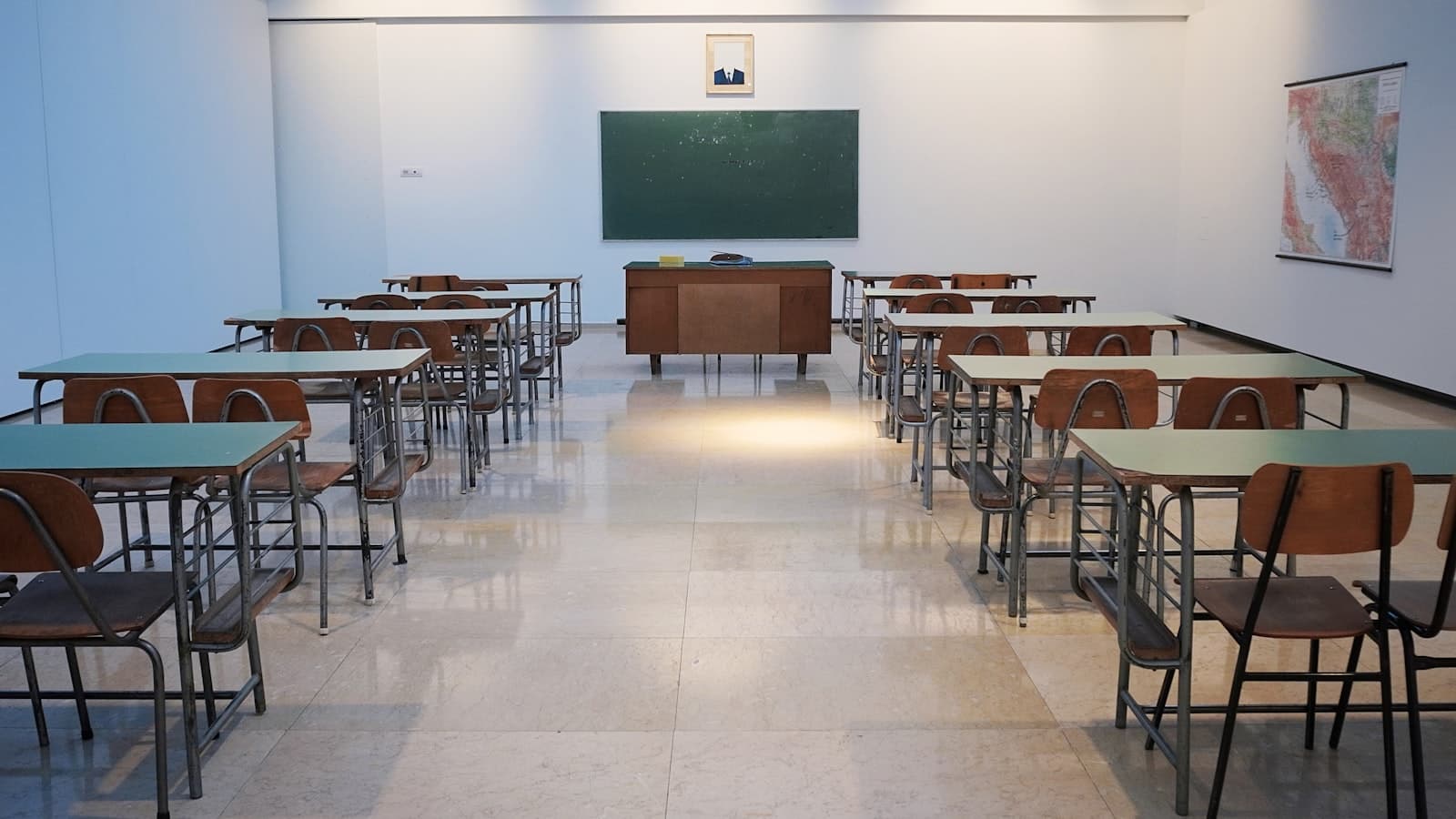 An empty classroom with rows of desks, chairs, and a blank chalkboard; no people or legible text.