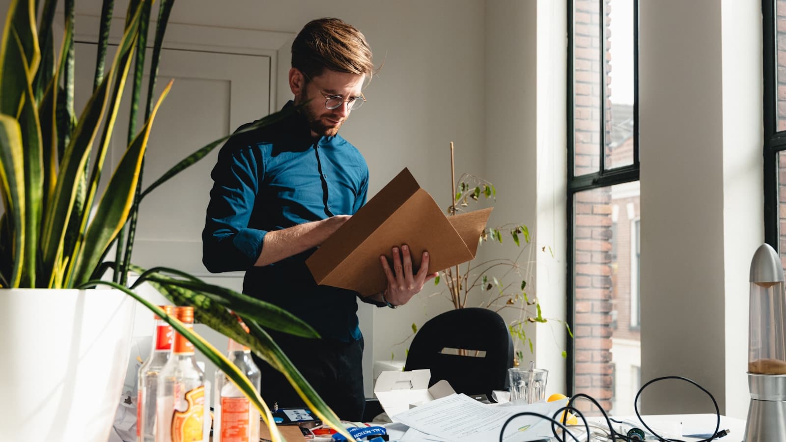 A man clearing out his office desk and packing a box, plants in background.