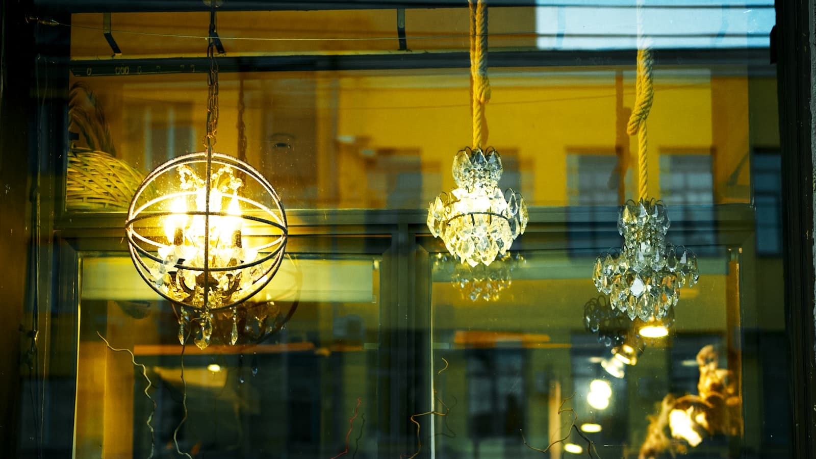 A boutique shop window at dusk with vases and hanging chandeliers reflected in the glass; no people or readable text.
