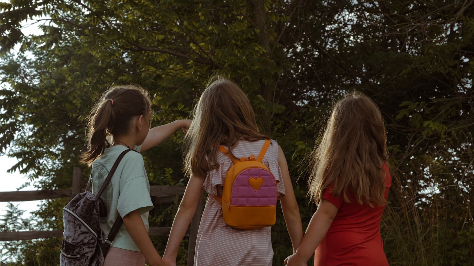 Three young girls holding hands walking away into trees.
