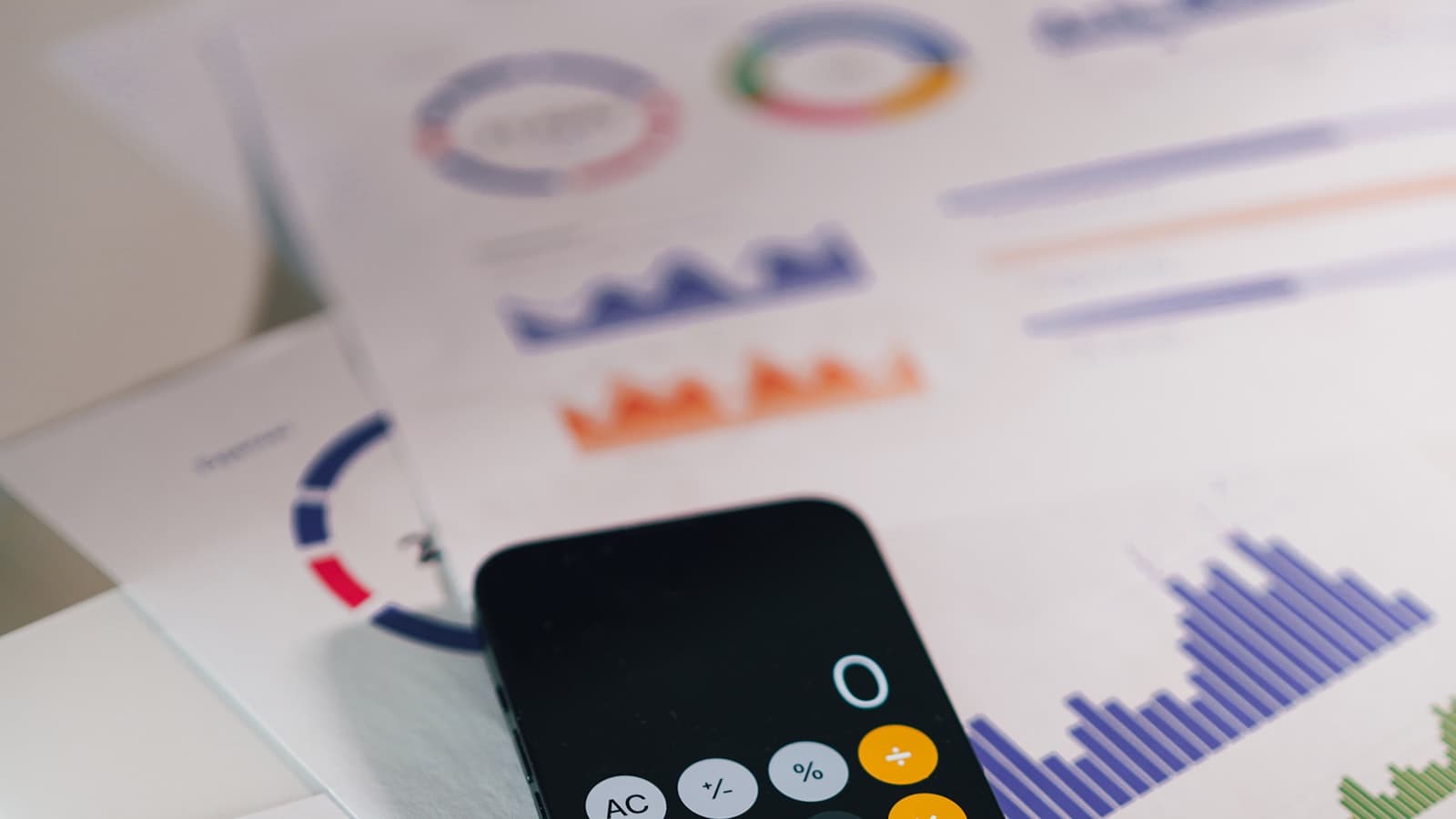 A phone calculator resting on top of printed financial charts and graphs